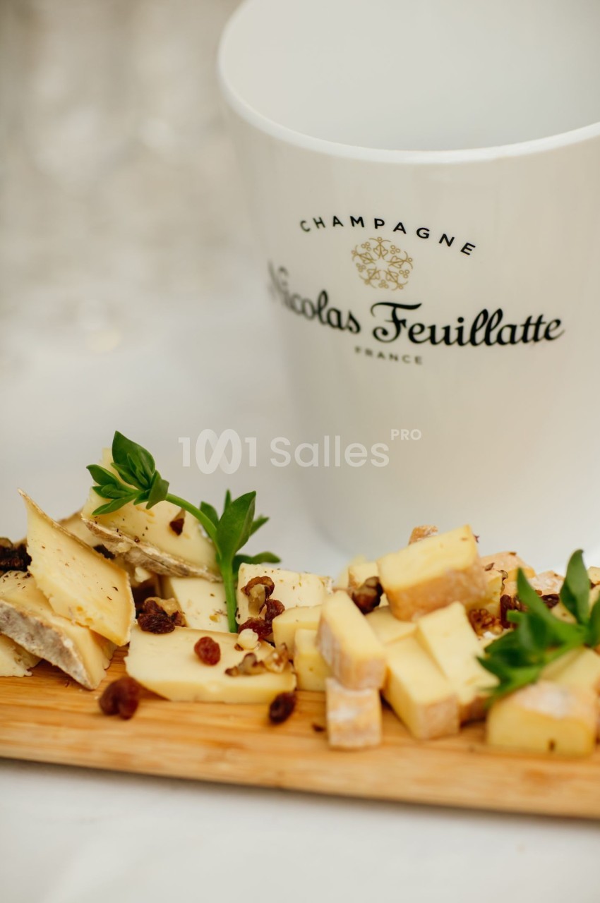 Plateau de fromages variés avec fruits secs, présenté sur une planche en bois, près d'un seau à champagne.