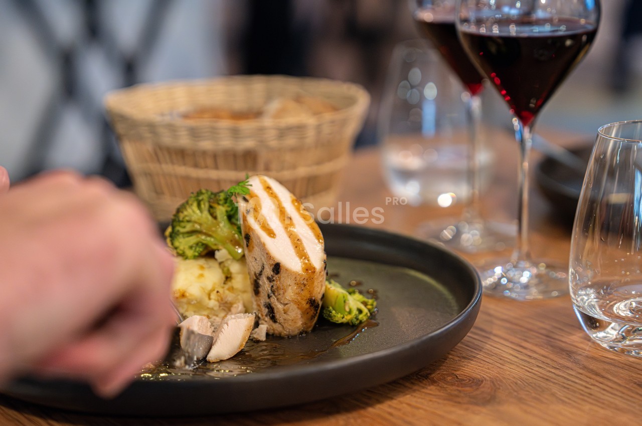 Assiette contenant un filet de poulet grillé, brocolis et purée, avec des verres de vin rouge en arrière-plan.