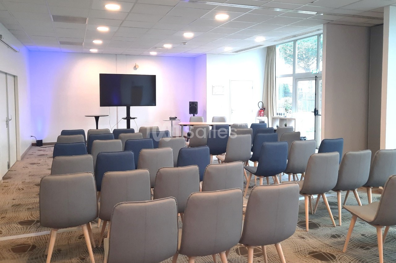 Salle de conférence lumineuse avec des rangées de chaises, un écran et un pupitre devant un mur éclairé en bleu.