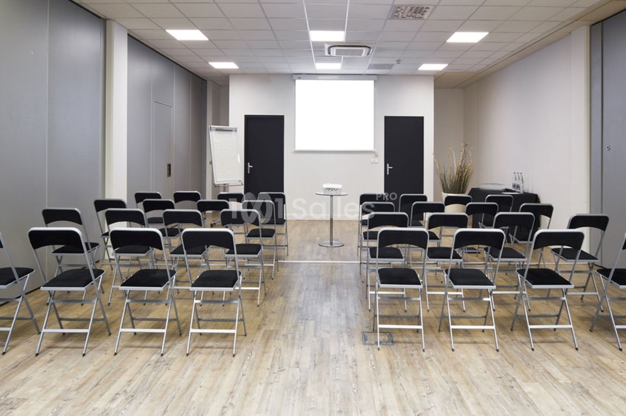 Salle de réunion avec des chaises noires alignées face à un écran de projection blanc et un pupitre central.