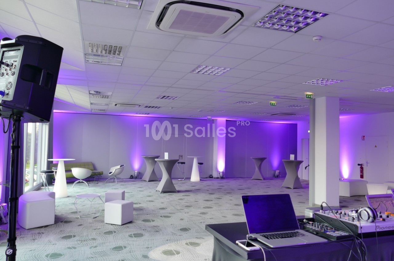 Salle de réception moderne avec éclairage violet, tables hautes, chaises design et matériel audio en premier plan.