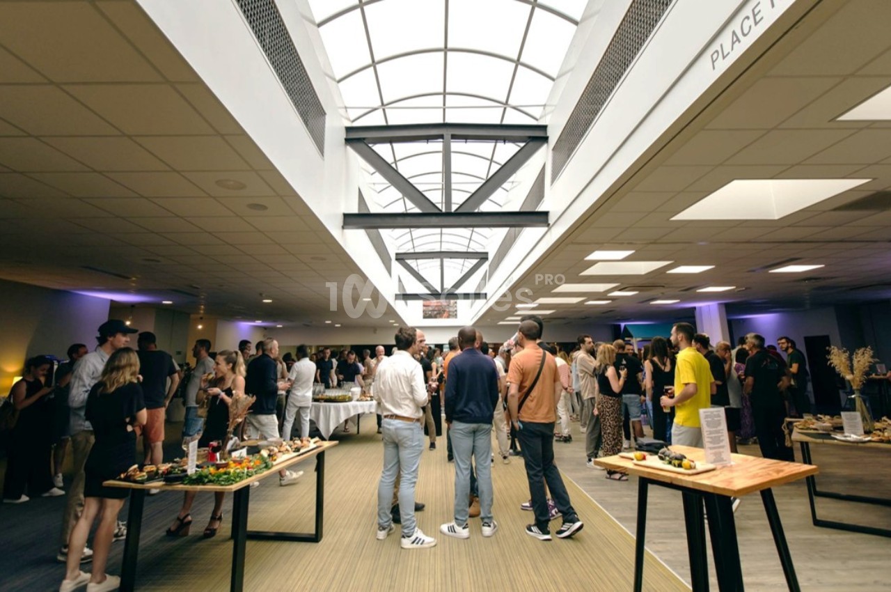 Des personnes rassemblées dans un hall lumineux avec des tables de buffet disposées autour.