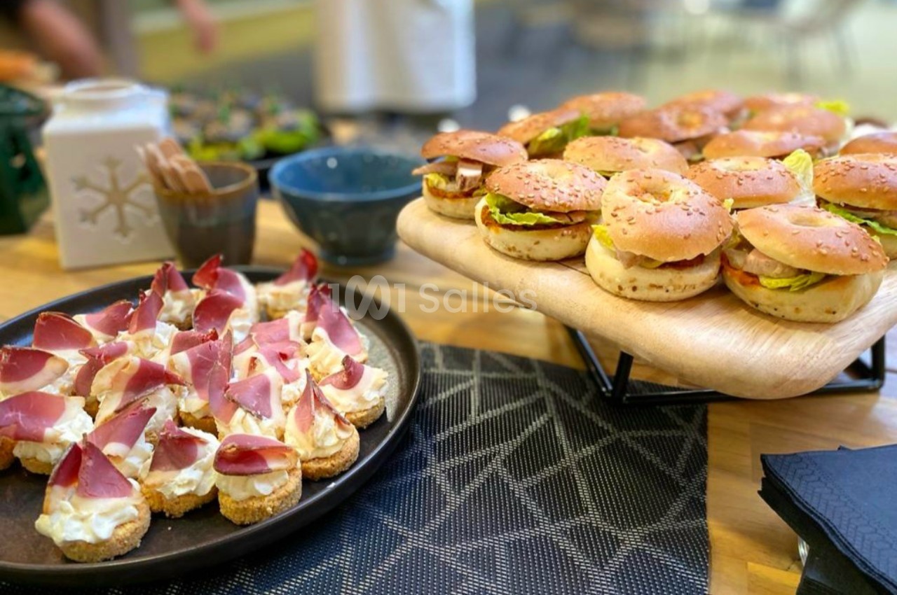 Plateau de mini-burgers au pain brioché et assiette de canapés au jambon cru et fromage frais sur une table.