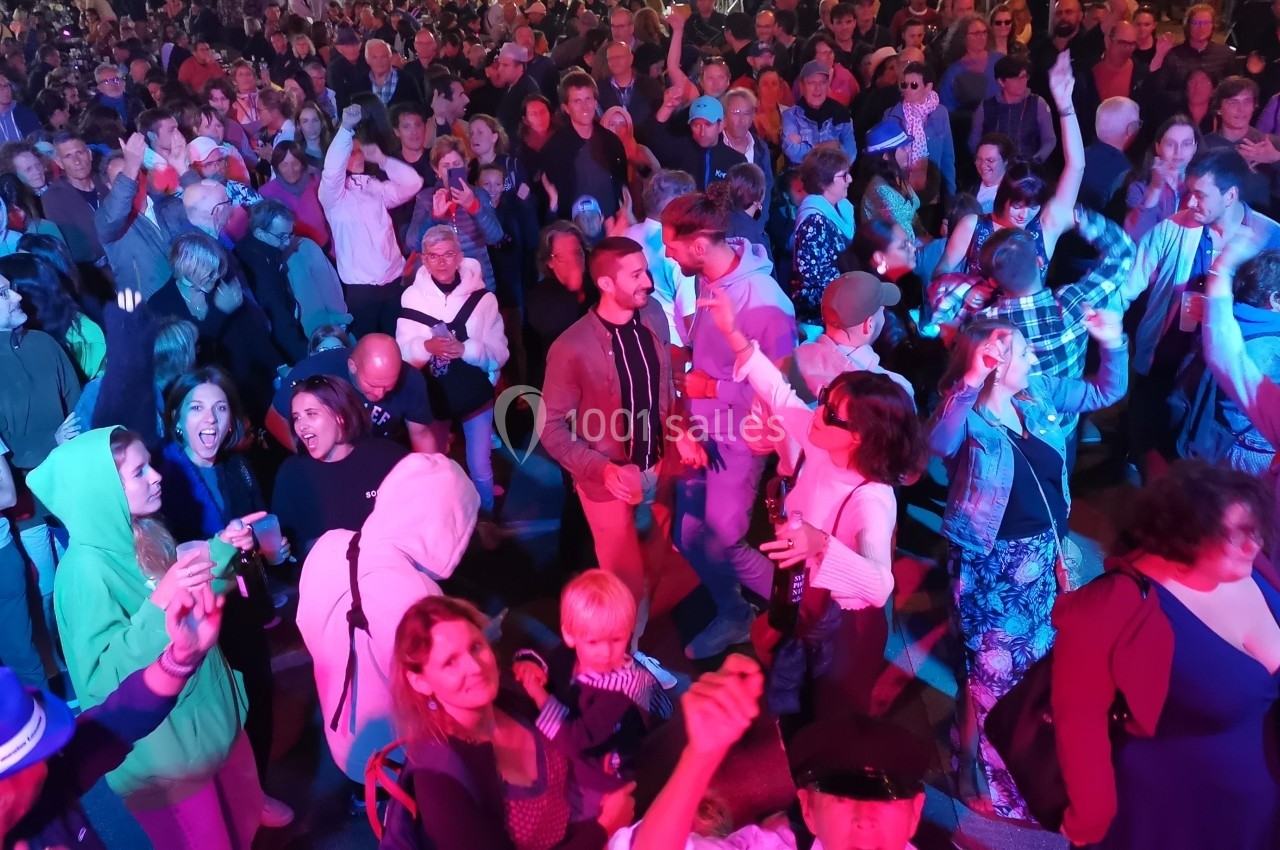 Foule de personnes dansant et profitant d'un événement festif en extérieur, éclairée par des lumières colorées.