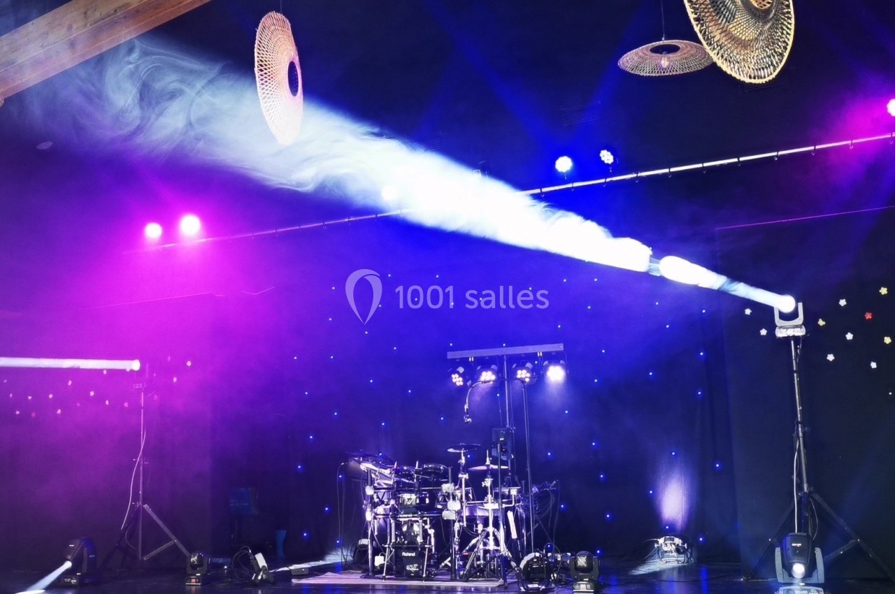 Scène de concert avec une batterie éclairée par des projecteurs colorés et un fond étoilé.