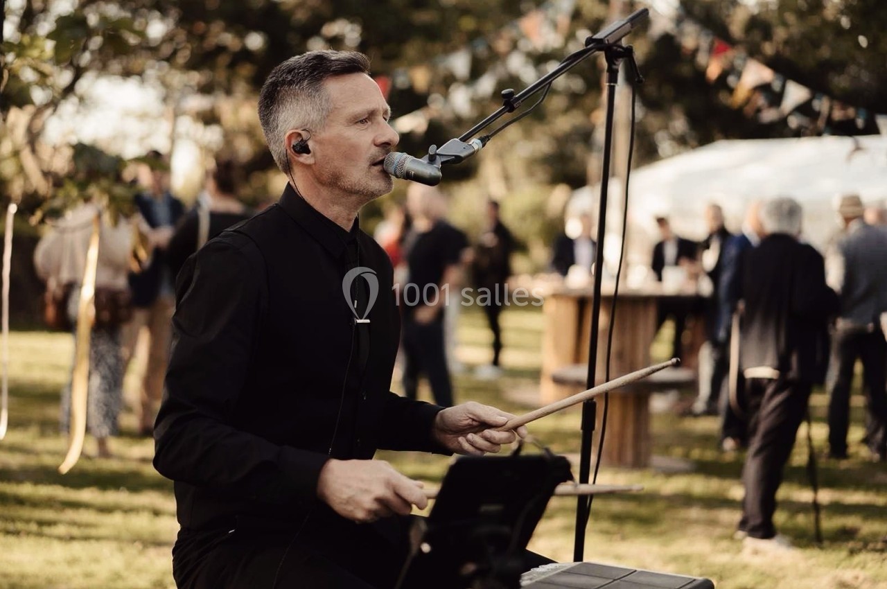 Un musicien joue de la batterie et chante au micro lors d'un événement en plein air.