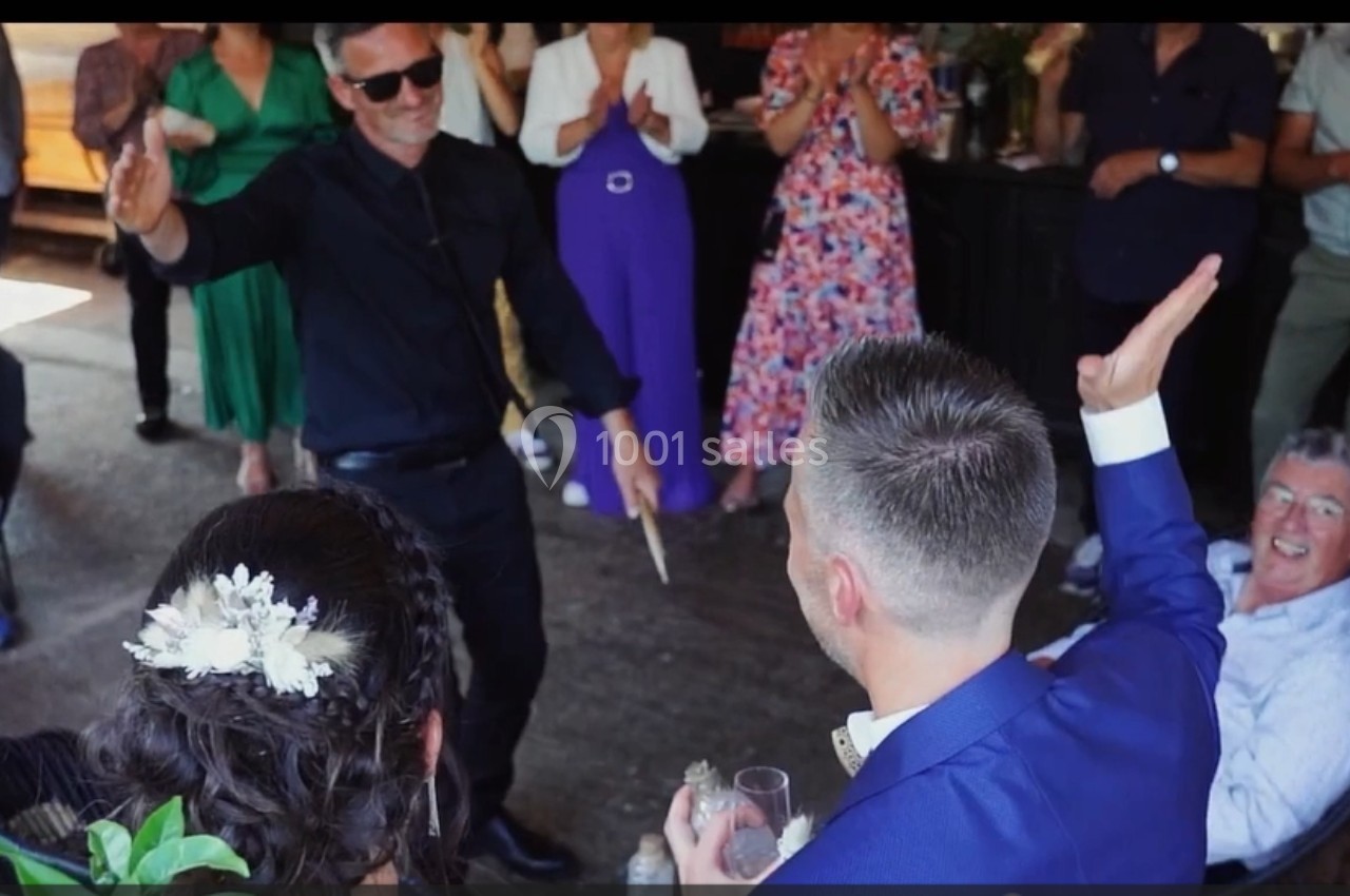 Un homme en noir danse devant un groupe de personnes applaudissant lors d'un événement festif.