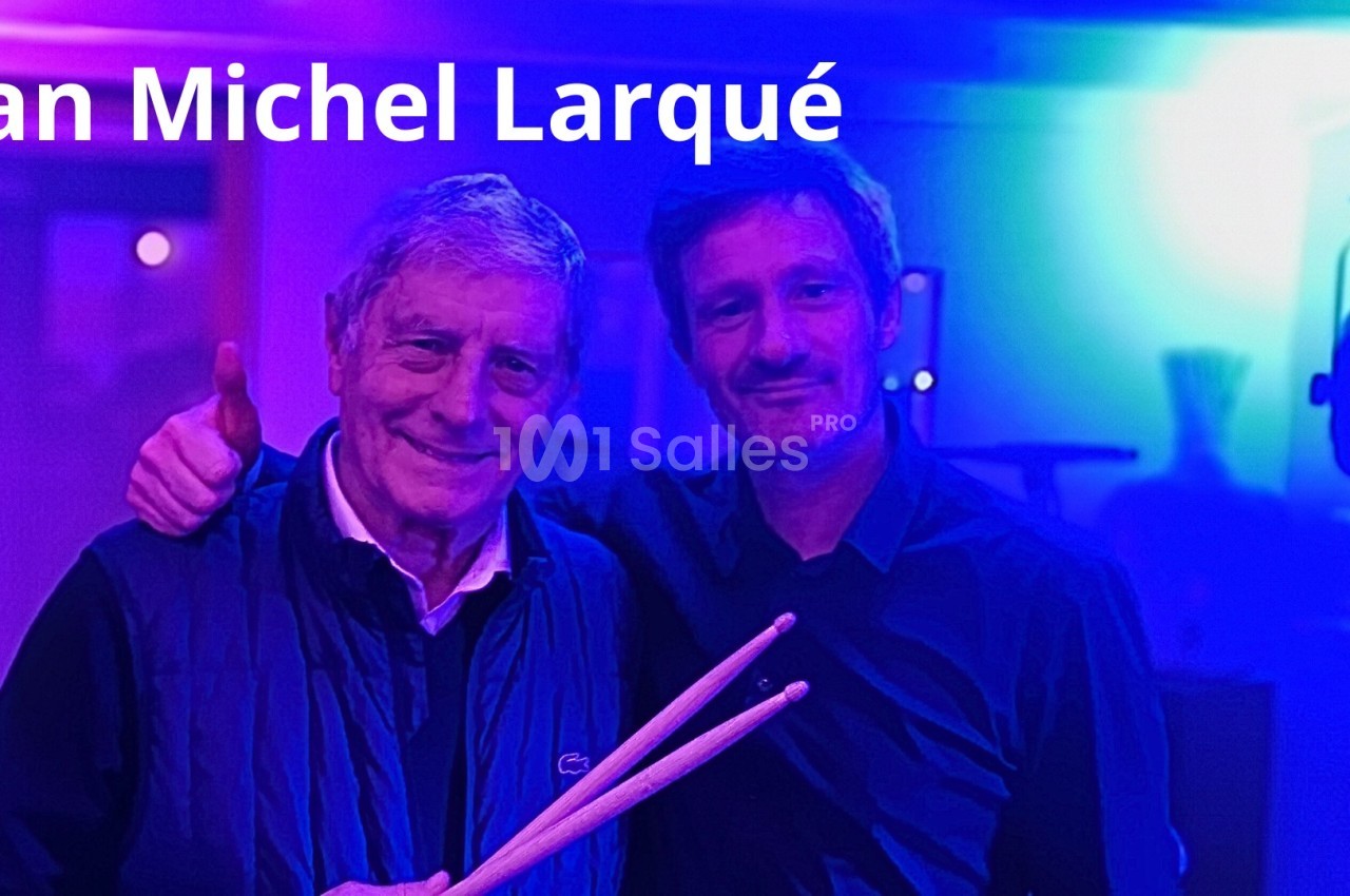 Deux hommes posent ensemble dans une ambiance lumineuse bleutée, l'un tenant des baguettes de batterie.
