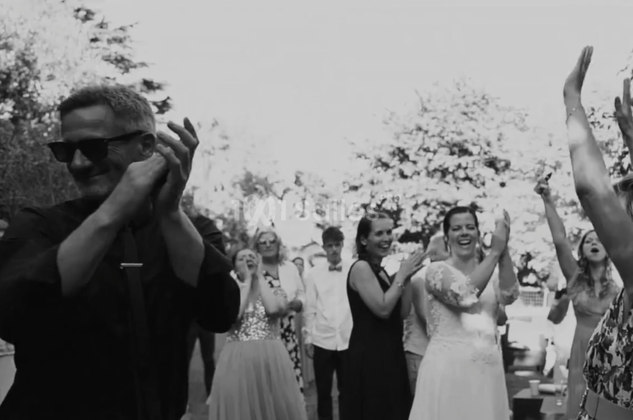 Des invités applaudissent et sourient lors d'une célébration en plein air, avec une mariée au centre de la scène.