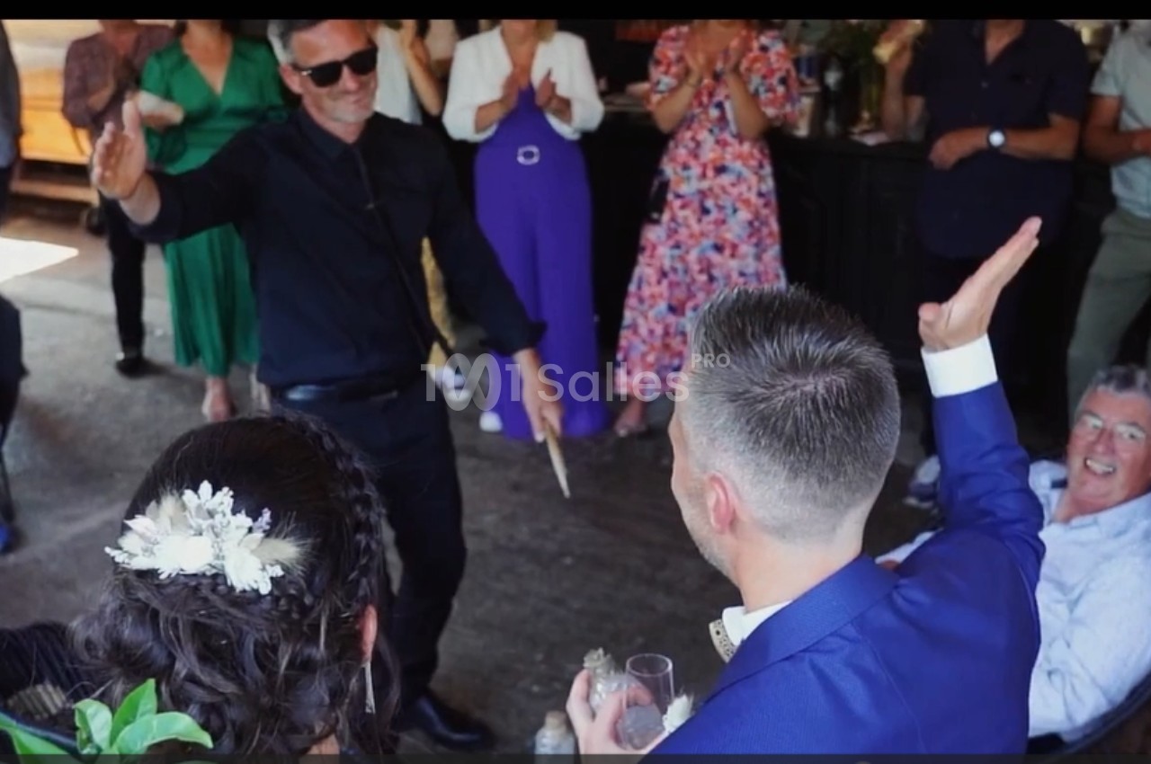 Un homme en noir danse devant un groupe de personnes applaudissant lors d'un événement festif.