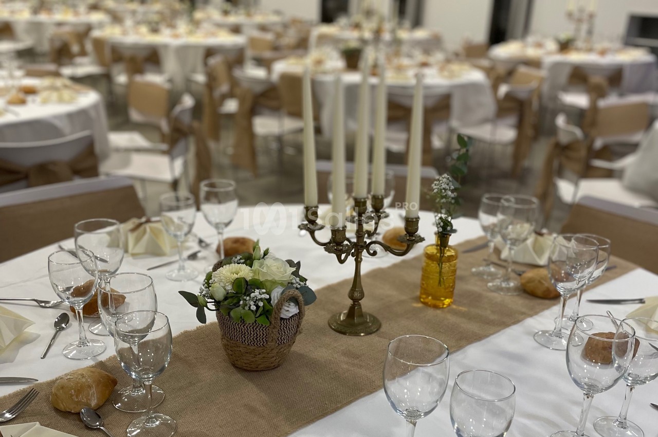 Salle de réception décorée avec des tables rondes, nappes blanches, chandeliers et compositions florales.