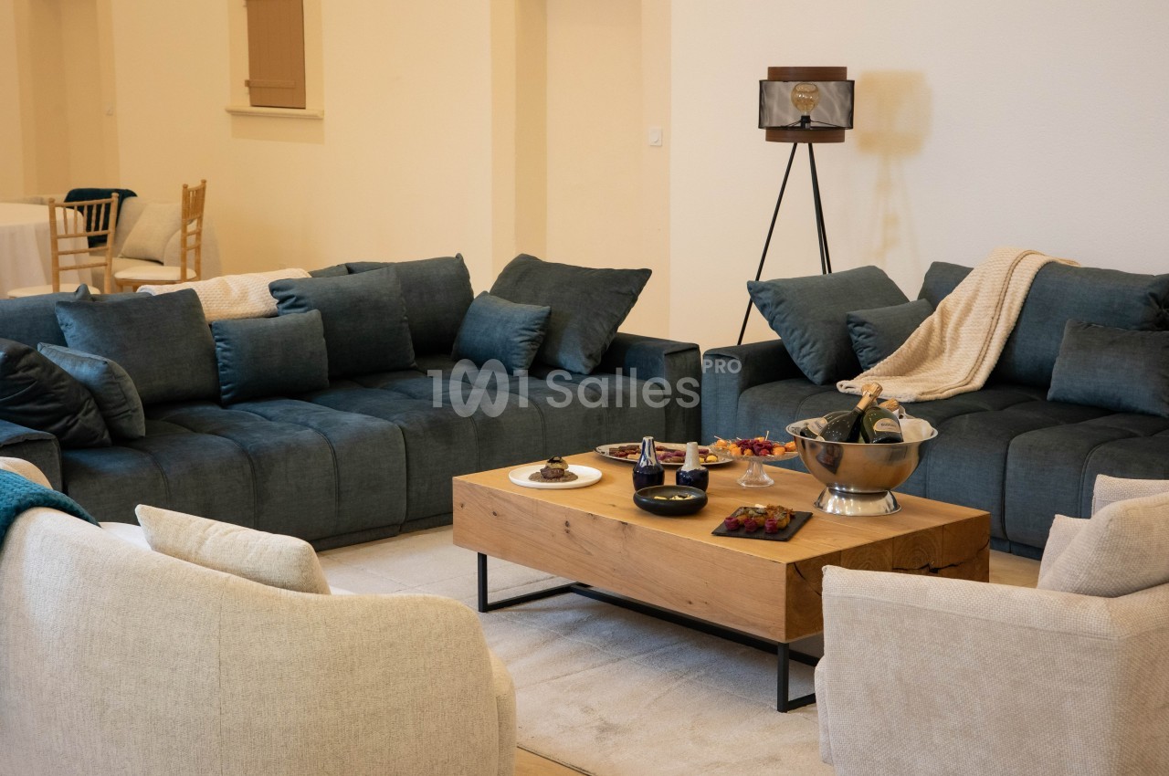Salon avec deux canapés bleu foncé, deux fauteuils beiges, une table basse en bois et des collations disposées dessus.