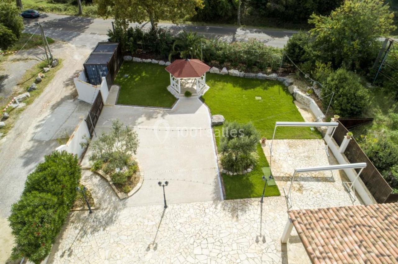 Vue aérienne d'une cour avec un kiosque central, pelouse, allée pavée et végétation environnante.