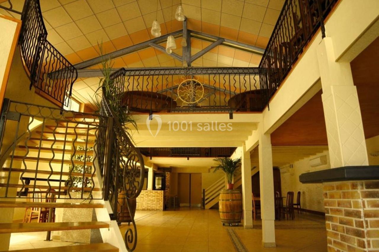 Intérieur d'une salle avec mezzanine, escaliers en fer forgé, poutres apparentes et décorations en bois et pierre.
