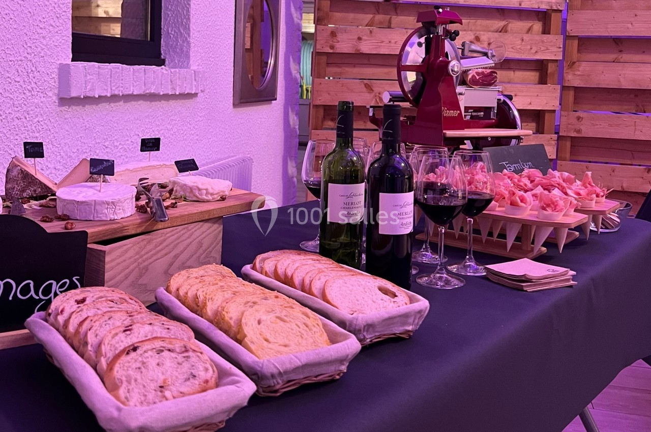 Table garnie de pain, fromages, charcuterie, bouteilles de vin et verres dans un décor intérieur chaleureux.