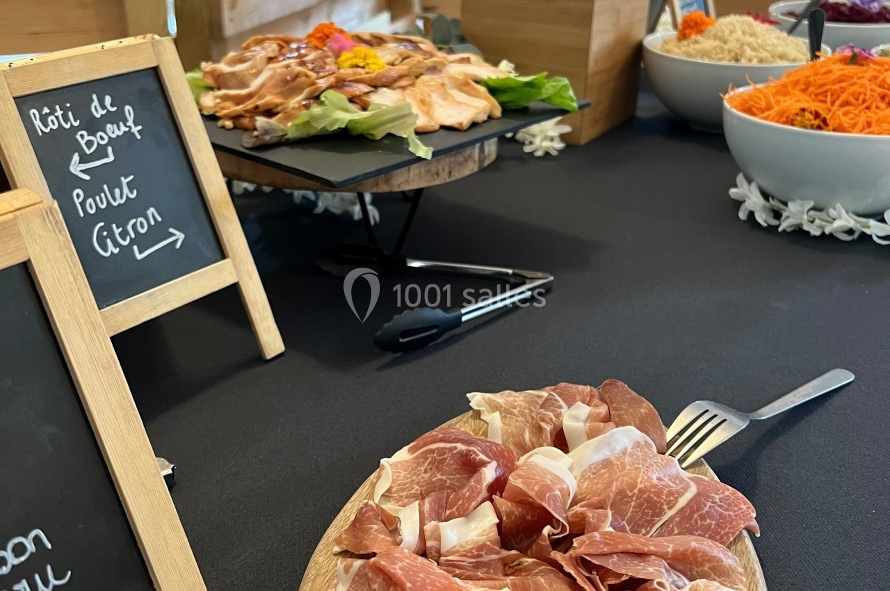 Plateau de charcuterie avec du jambon cru au premier plan, accompagné de plats variés en arrière-plan.