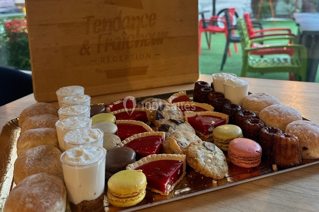 Plateau de pâtisseries variées comprenant macarons, cannelés, tartelettes, choux et autres desserts sur une table en bois.