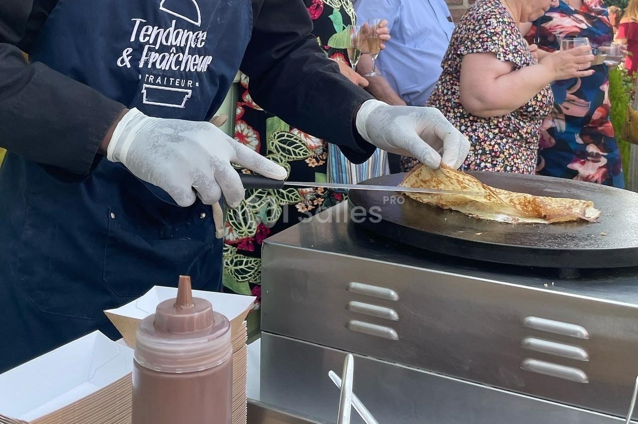 Un cuisinier prépare une crêpe sur une plaque chauffante lors d'un événement en plein air.