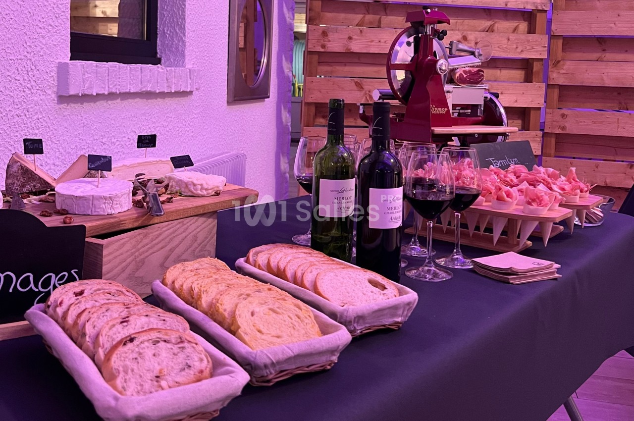 Table garnie de pain, fromages, charcuterie, bouteilles de vin et verres dans un décor intérieur chaleureux.