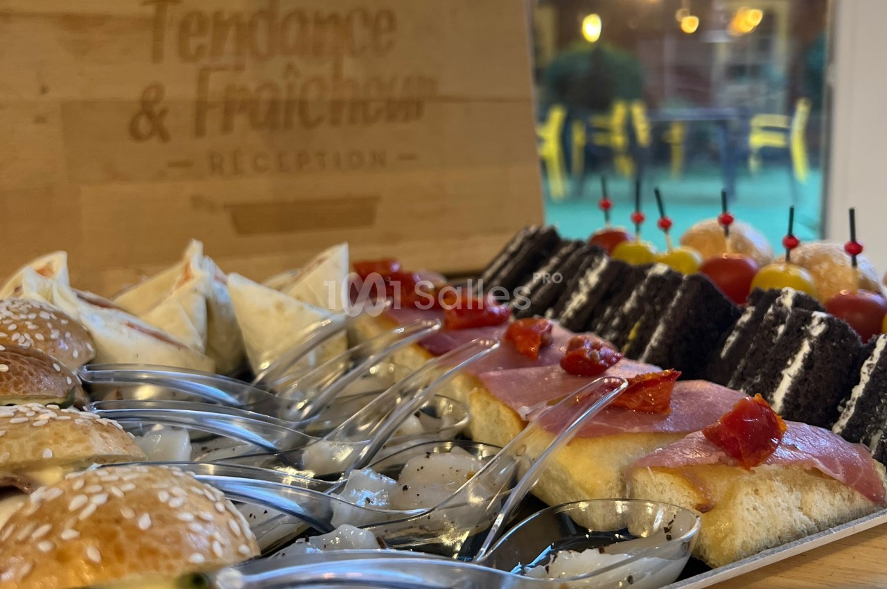 Plateau de bouchées variées comprenant mini-sandwichs, wraps, gâteaux et verrines, présenté sur une table.