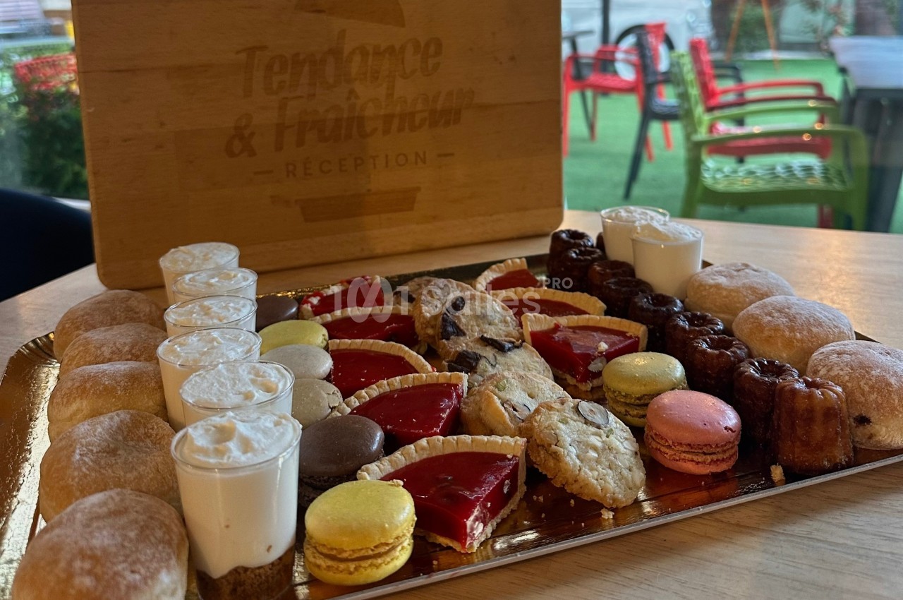 Plateau de pâtisseries variées comprenant macarons, cannelés, tartelettes, choux et autres desserts sur une table en bois.
