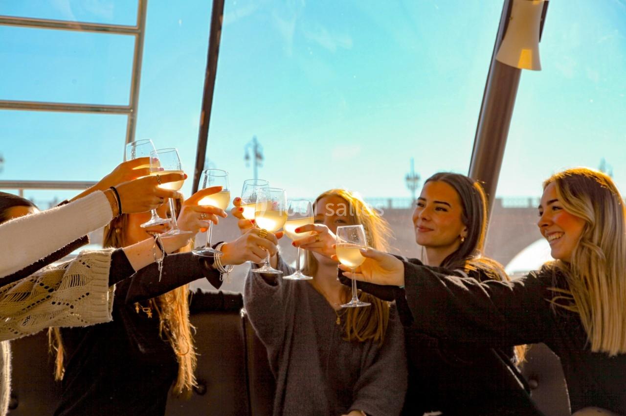 Un groupe de jeunes femmes trinque avec des verres de vin blanc dans un cadre ensoleillé.
