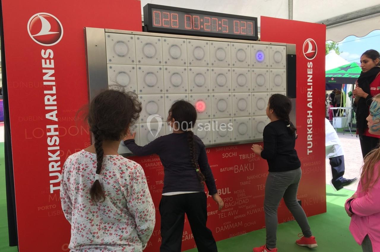 Des enfants jouent à un jeu interactif lumineux sur un mur sous une tente, avec des panneaux Turkish Airlines en arrière…