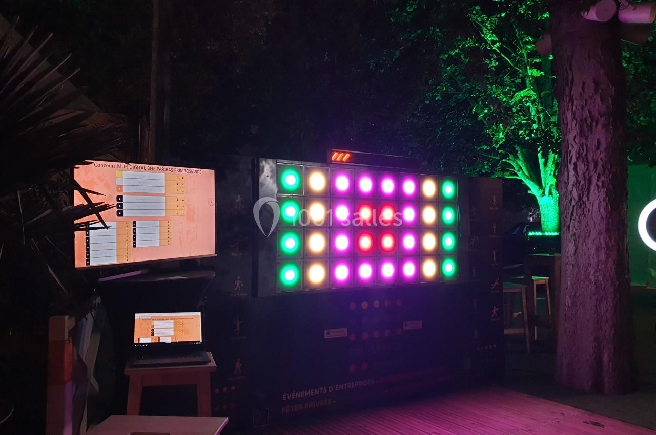 Mur interactif lumineux avec des motifs colorés, accompagné d'écrans et d'un ordinateur dans un environnement extérieur…