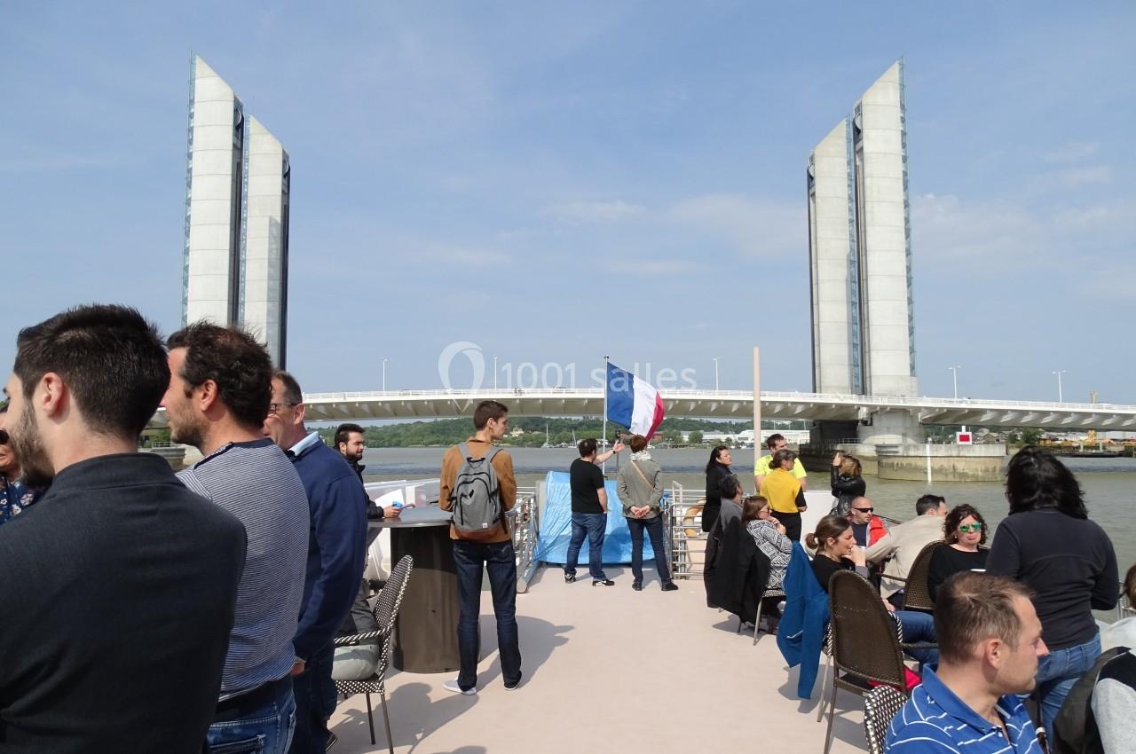 Des personnes discutent sur le pont d'un bateau devant le pont levant Jacques Chaban-Delmas à Bordeaux.