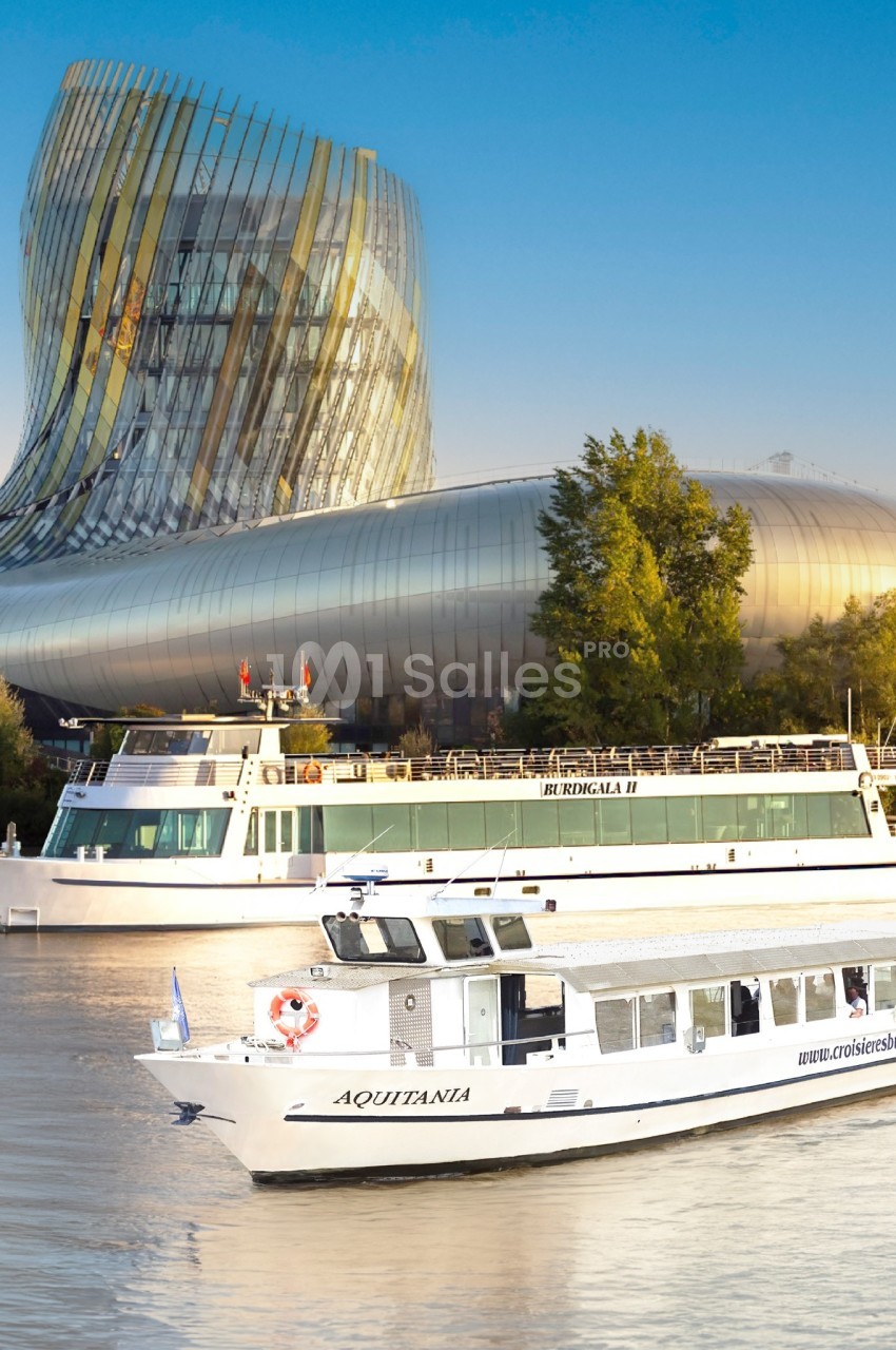 Deux bateaux de croisière naviguent sur une rivière devant un bâtiment moderne aux formes courbées.