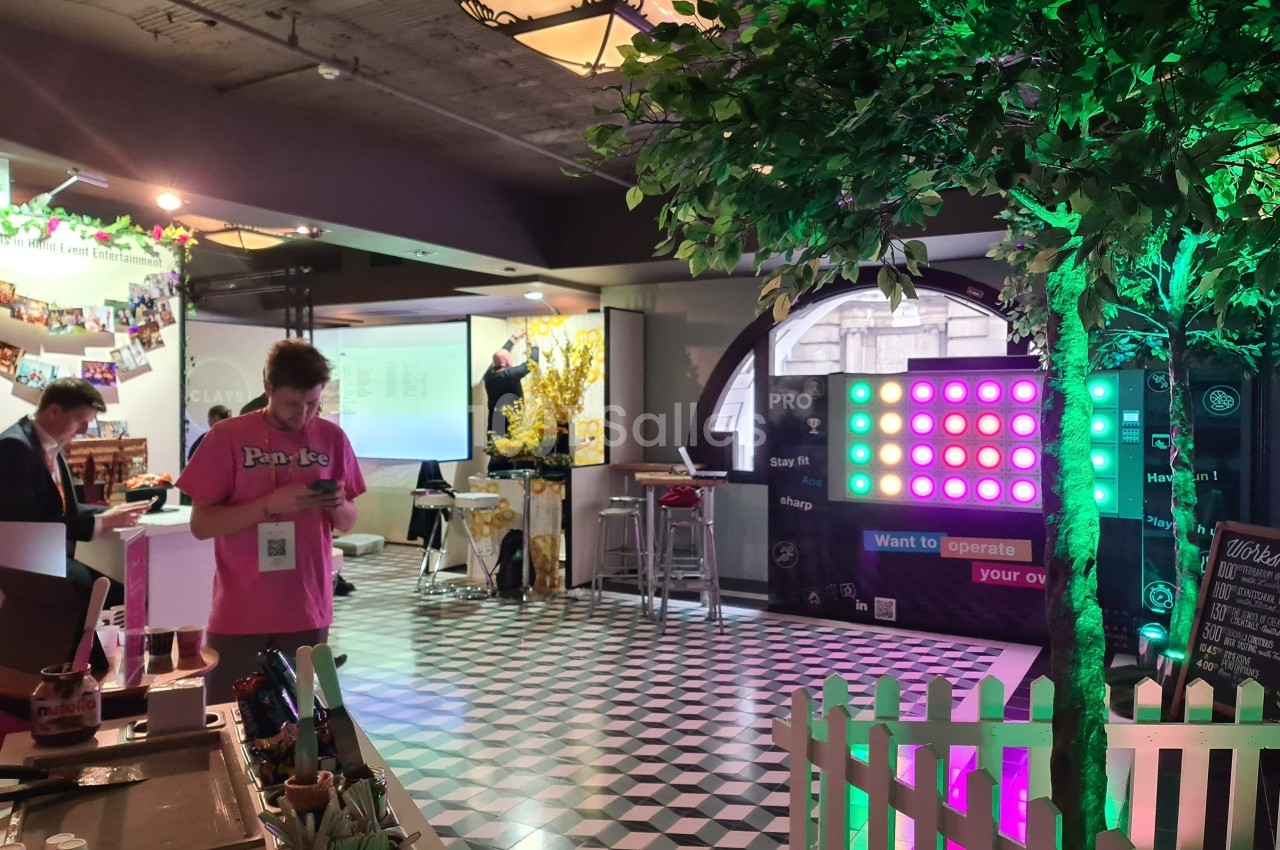 Un homme debout consulte son téléphone dans un espace intérieur décoré avec des lumières et des arbres artificiels.