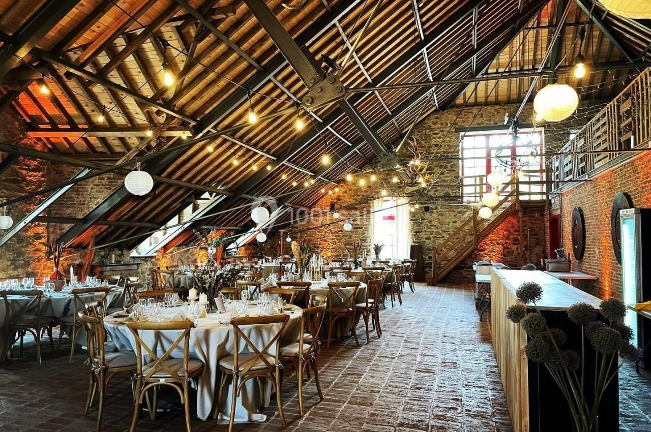 Salle de réception avec tables dressées, poutres apparentes, murs en pierre et éclairage chaleureux.