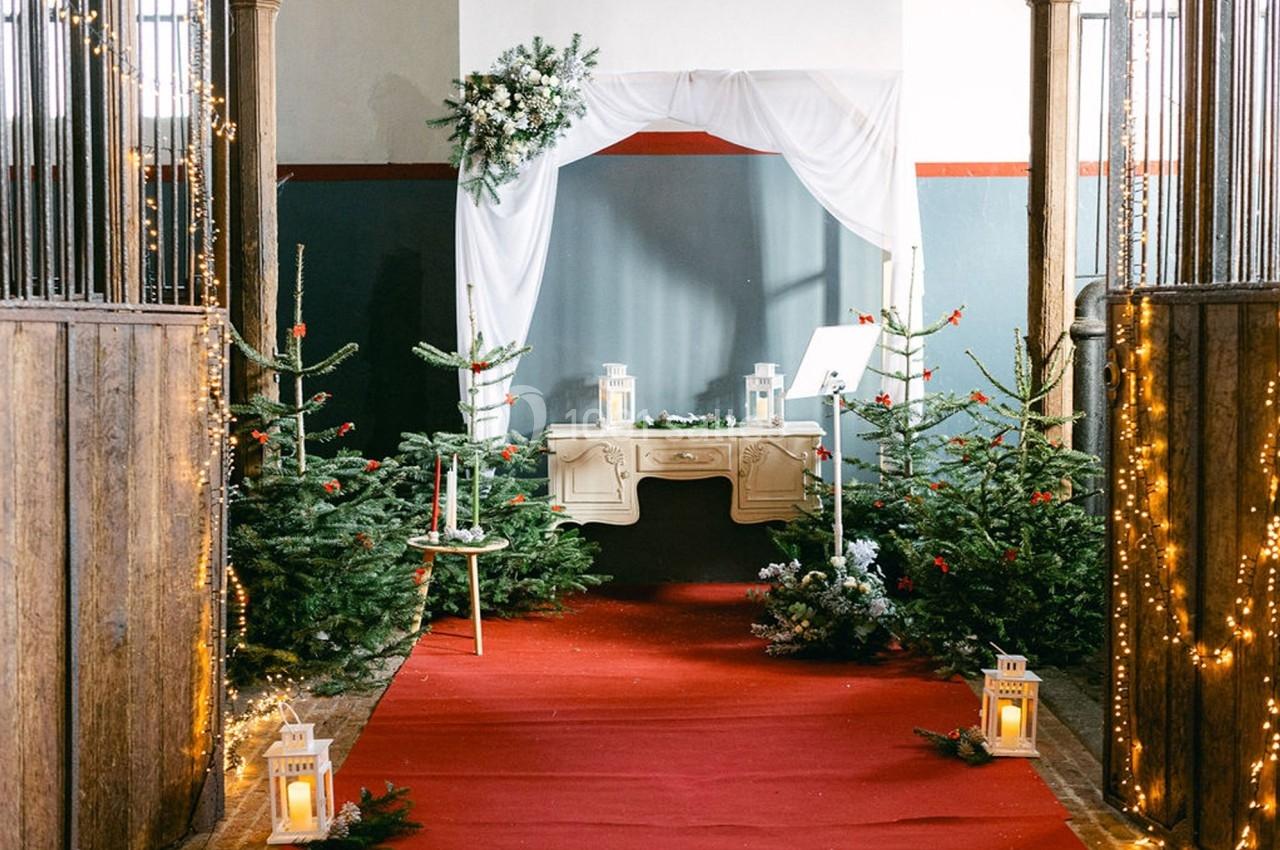 Allée décorée de sapins, guirlandes lumineuses et lanternes, menant à une table blanche sous un drapé festif.