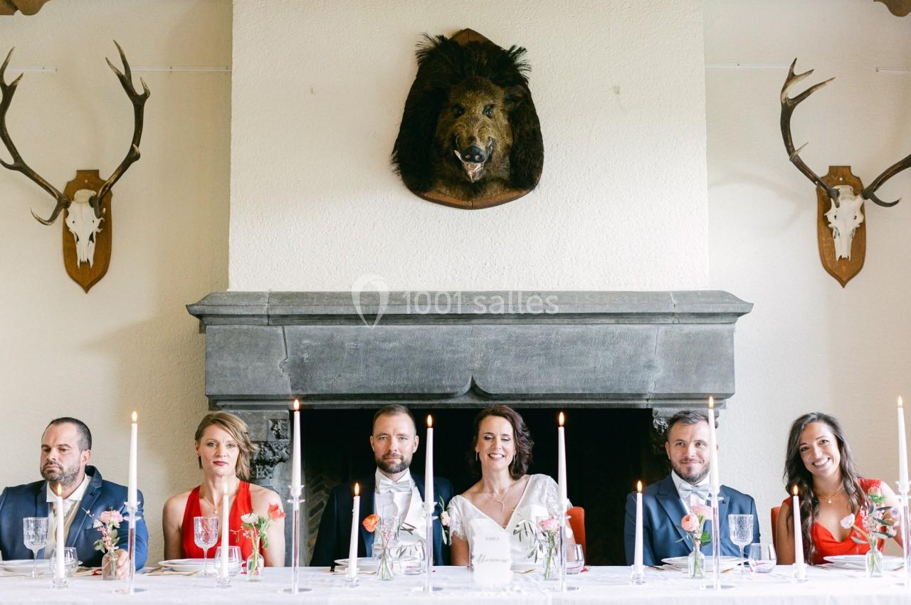 Un groupe de personnes assises à une table décorée, devant une cheminée ornée de trophées de chasse.