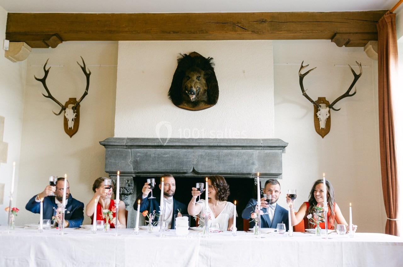 Des convives assis à une longue table lèvent leurs verres dans une salle décorée de trophées de chasse.