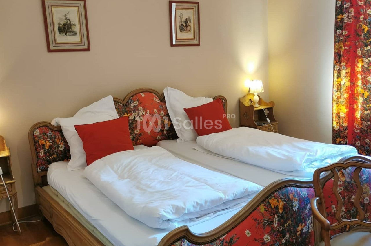 Chambre avec deux lits simples, tête de lit et textiles à motifs floraux, éclairée par des lampes de chevet.