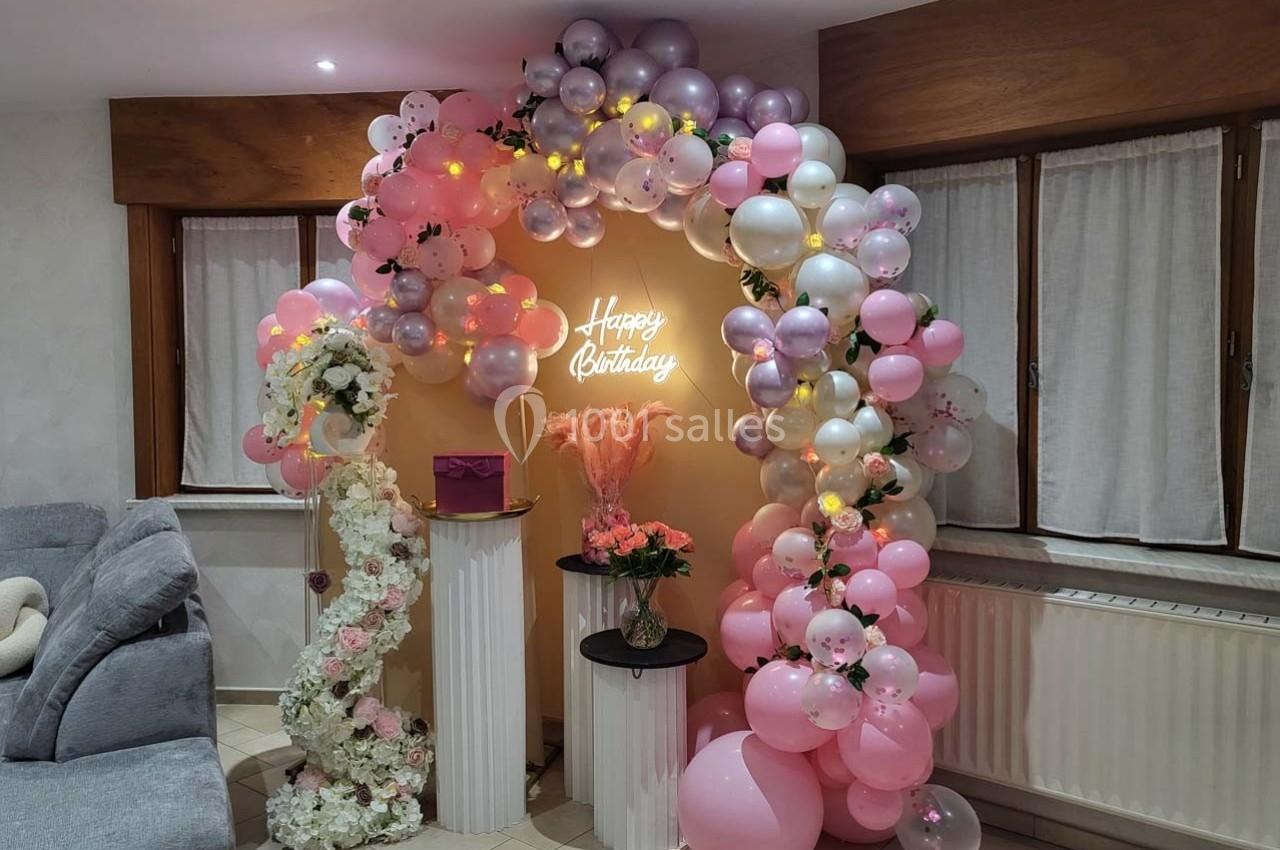 Arc de ballons roses, blancs et argentés avec une inscription lumineuse ’Happy Birthday’, décoré de fleurs et d'accessoires…
