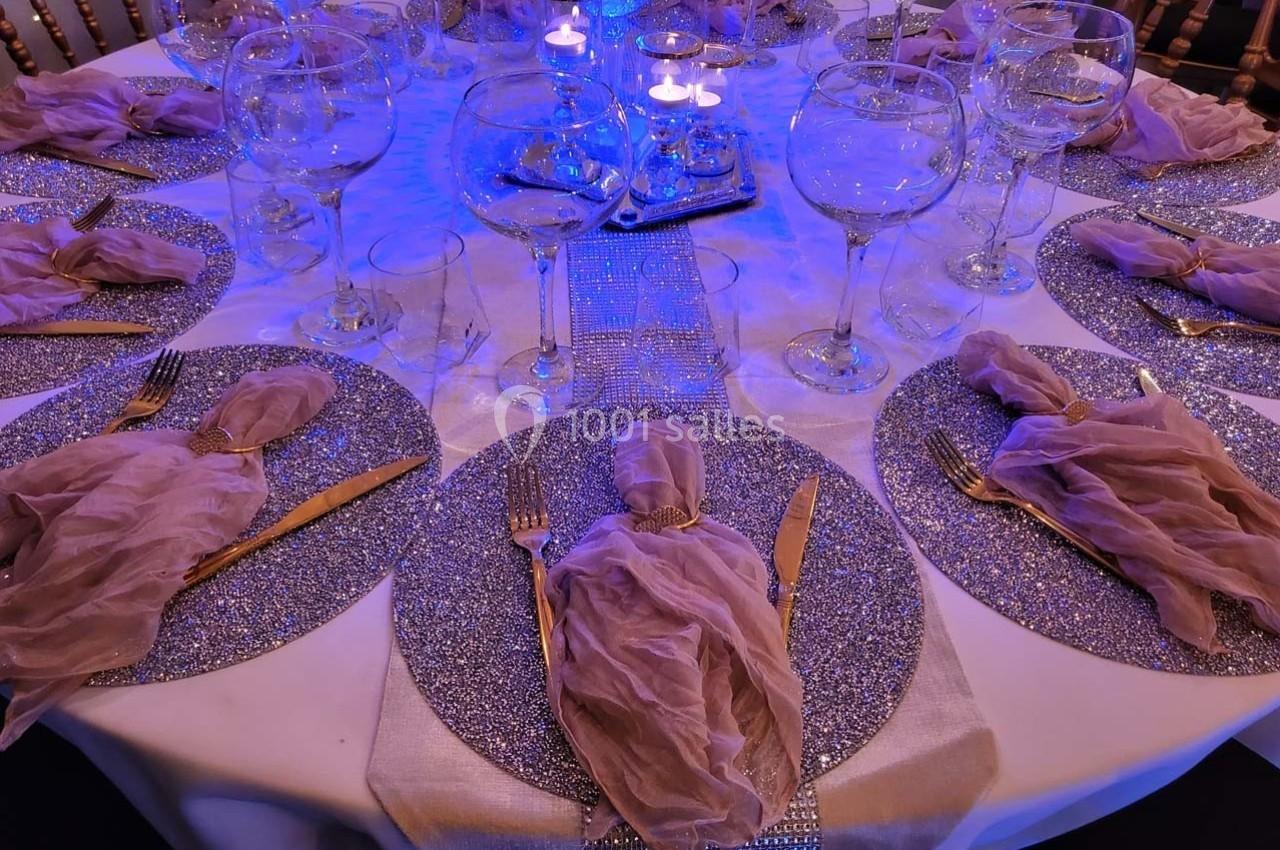Table élégamment dressée avec nappes scintillantes, serviettes en tissu rose et verres à vin sous un éclairage tamisé.