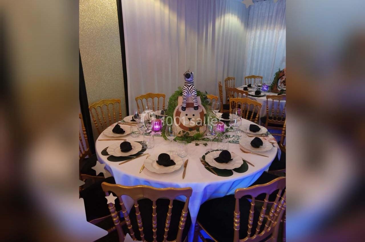 Table ronde décorée sur le thème safari avec un centre de table représentant un lion et des serviettes pliées en forme de…