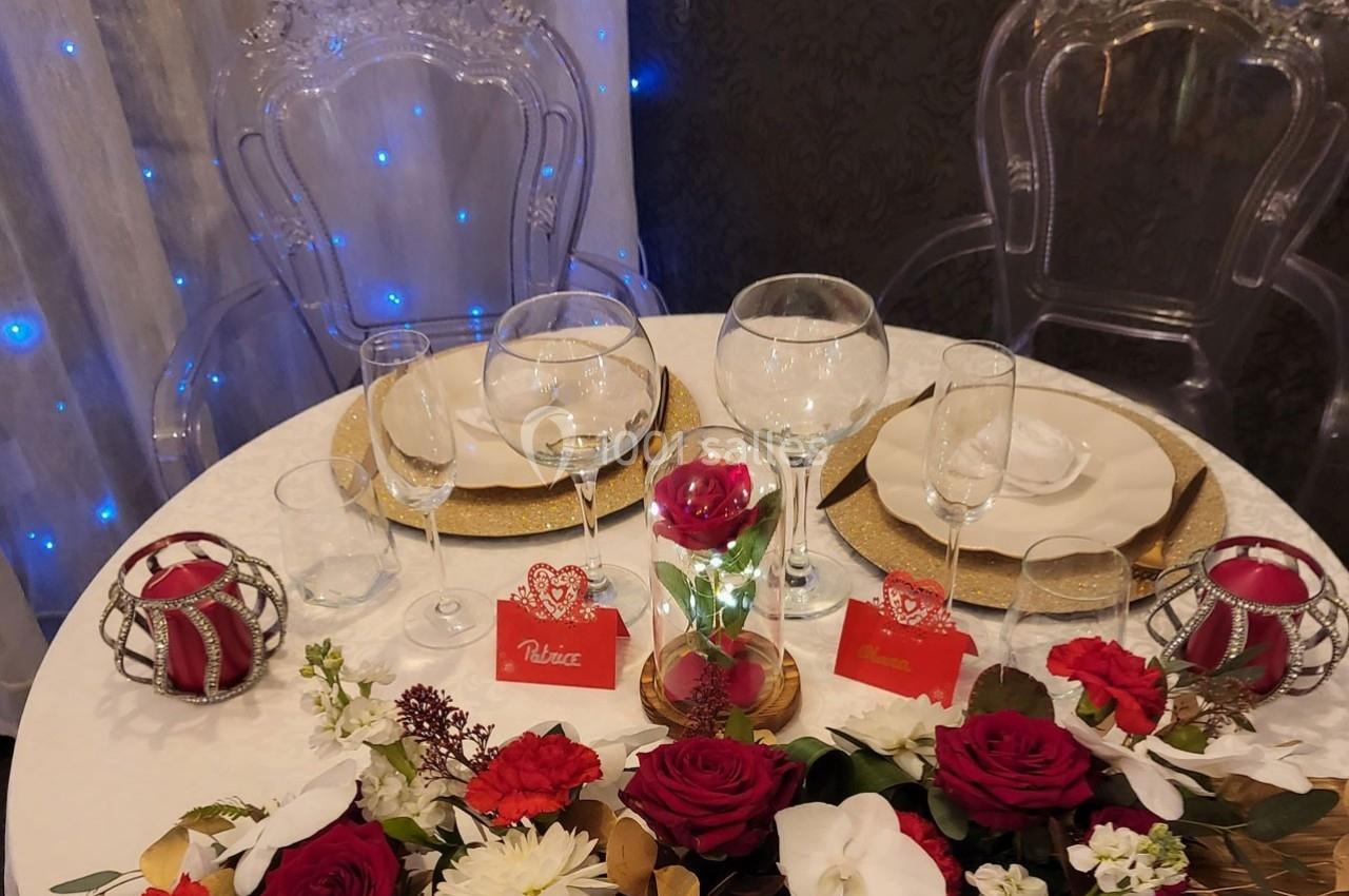 Table décorée pour un dîner, avec vaisselle élégante, fleurs rouges et blanches, et cartes de place personnalisées.