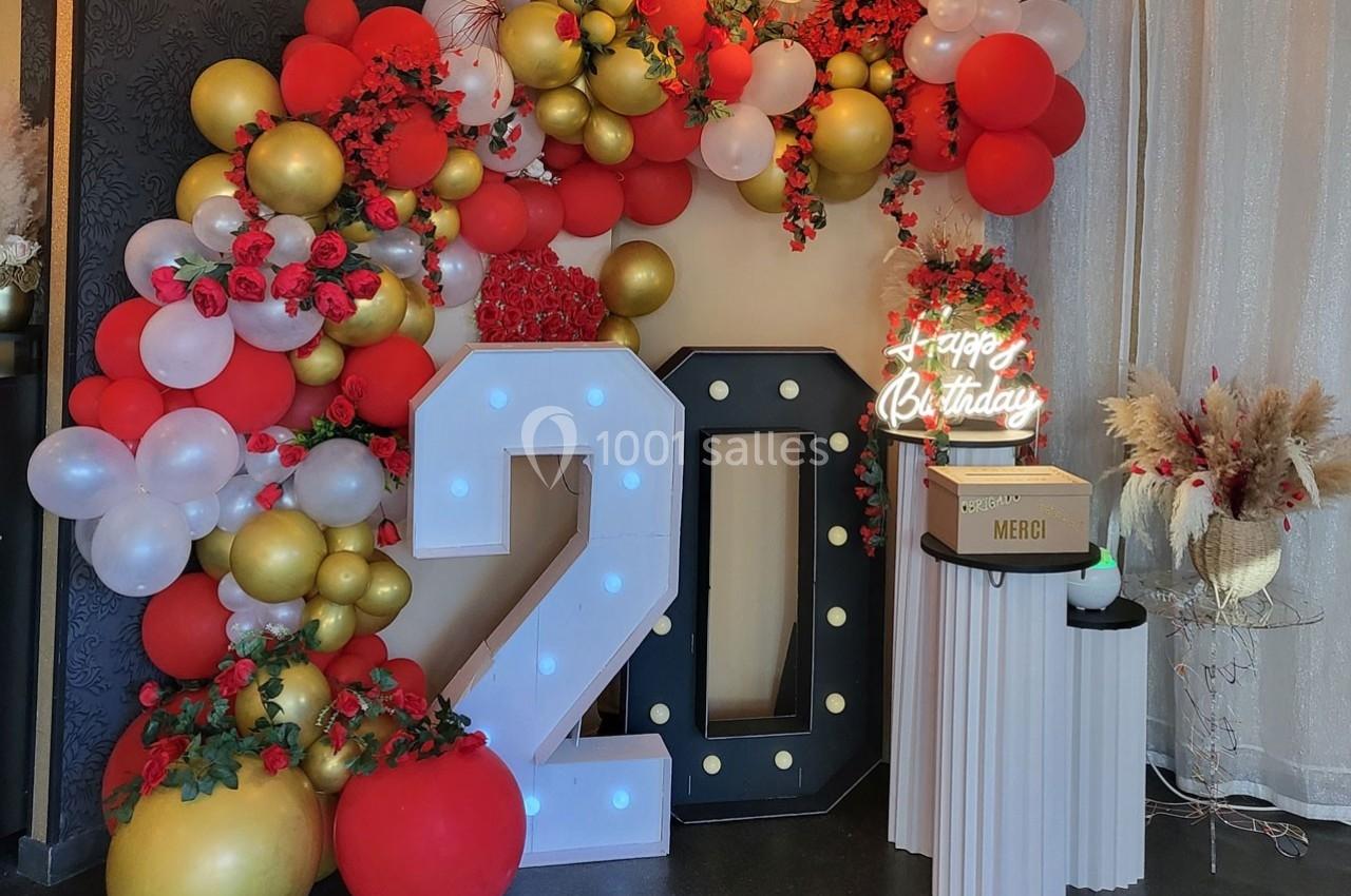Décoration festive avec ballons rouges, blancs et dorés, chiffre 20 lumineux, et panneau ’Happy Birthday’ éclairé.