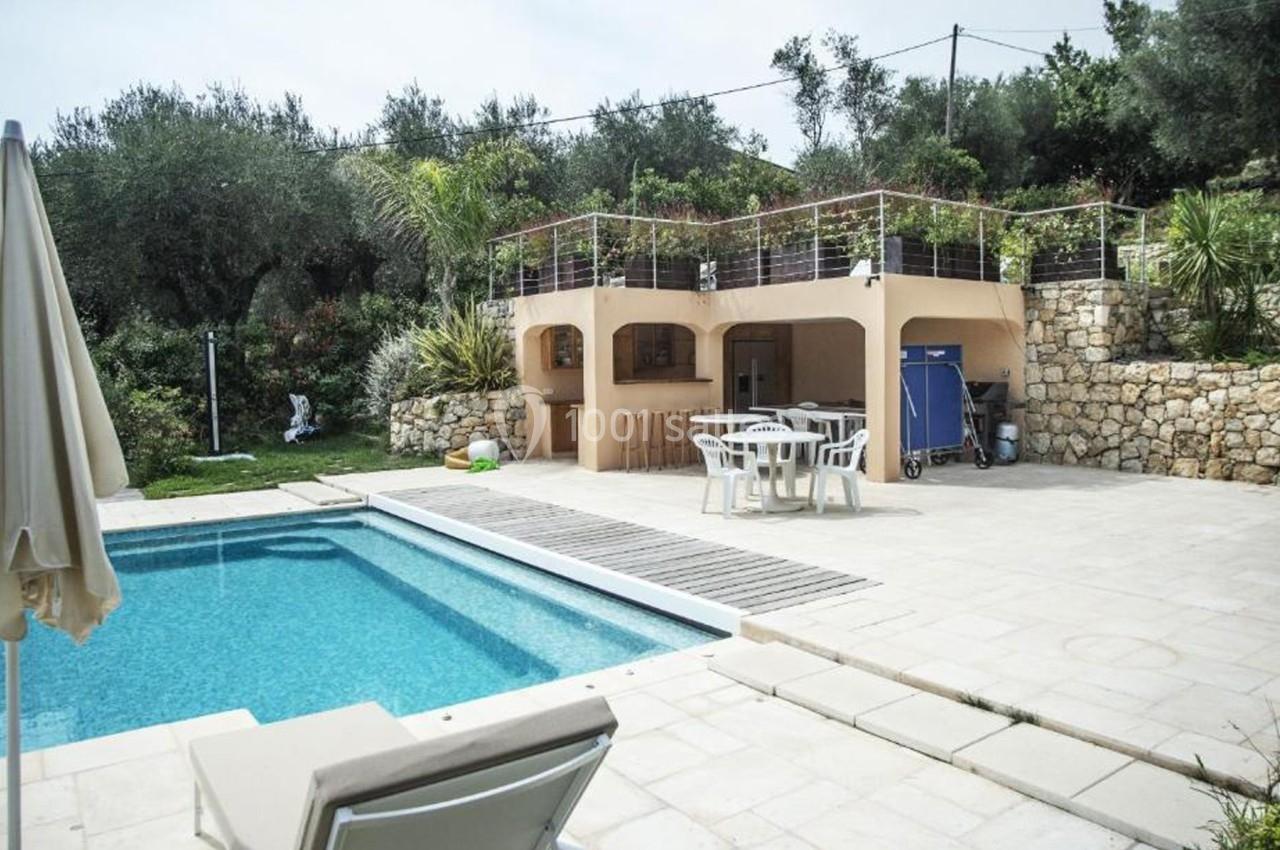 Terrasse avec piscine, transat, parasol, mobilier de jardin et cuisine extérieure entourée de végétation méditerranéenne.