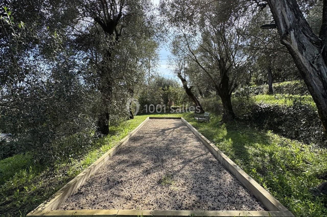 Terrain de pétanque en gravier entouré d'arbres et de végétation sous un ciel ensoleillé.