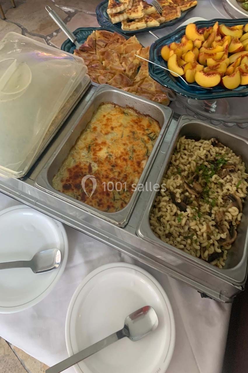 Buffet avec gratin, pâtes aux champignons, tarte et fruits frais, présenté dans des plats en inox et assiettes blanches.