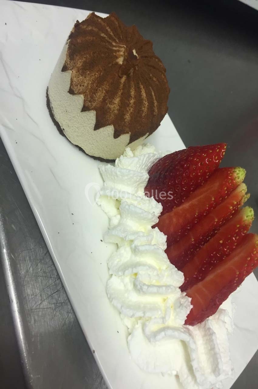 Un dessert composé d'une mousse au chocolat saupoudrée de cacao, accompagné de fraises tranchées et de chantilly.