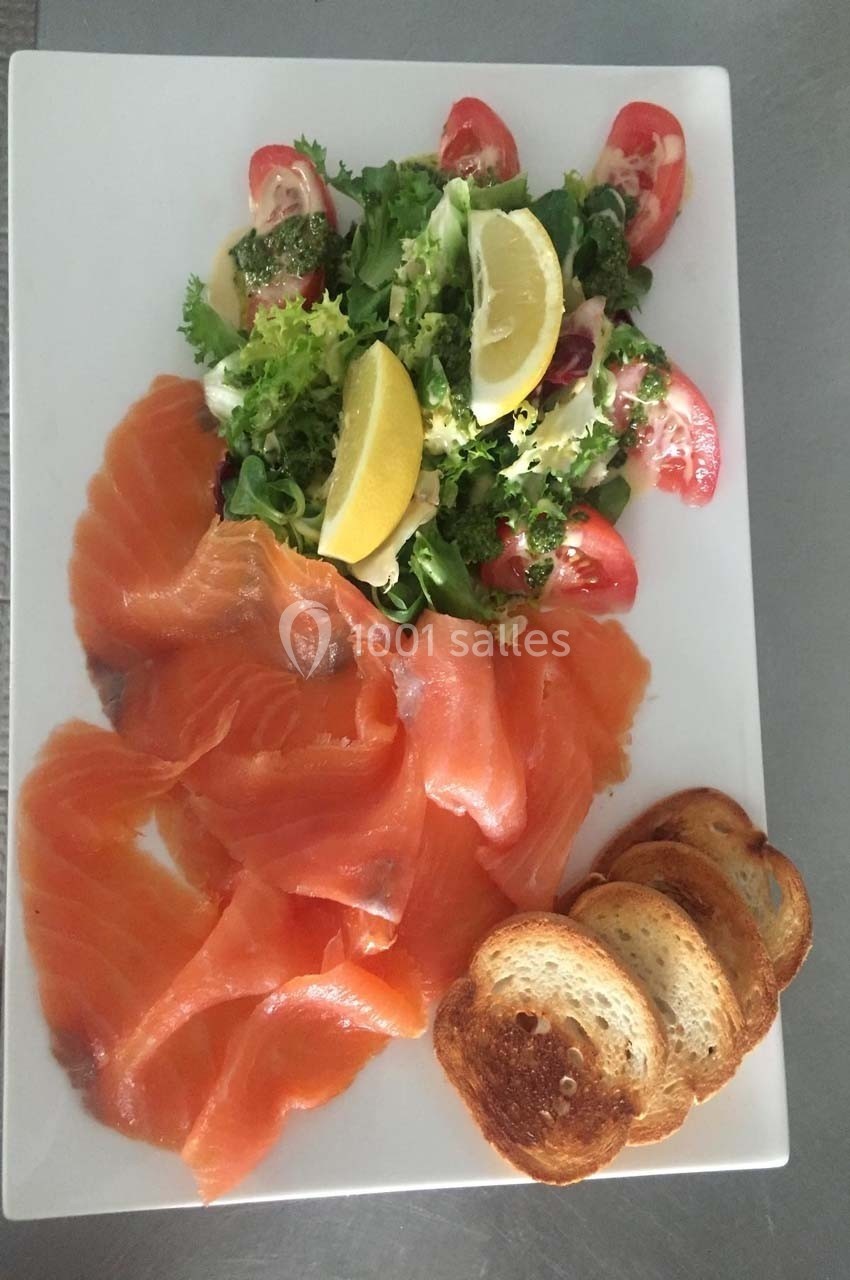 Assiette avec tranches de saumon fumé, salade verte garnie de tomates et citron, accompagnée de toasts grillés.