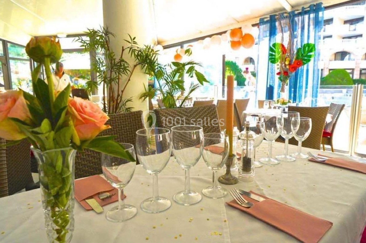 Table dressée avec des verres, serviettes roses et décoration florale dans un restaurant lumineux avec vue extérieure.