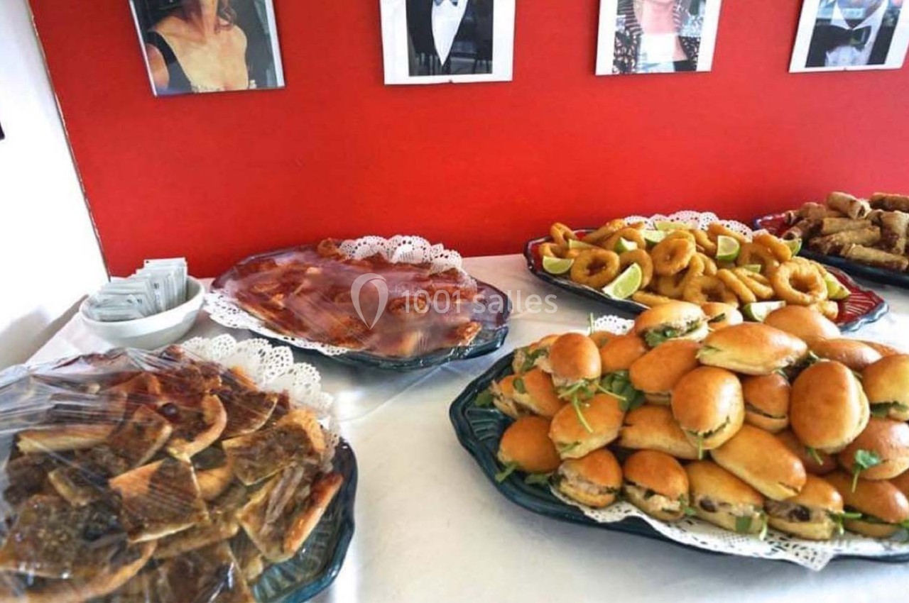 Plateaux de viennoiseries, sandwichs et beignets disposés sur une table devant un mur rouge.