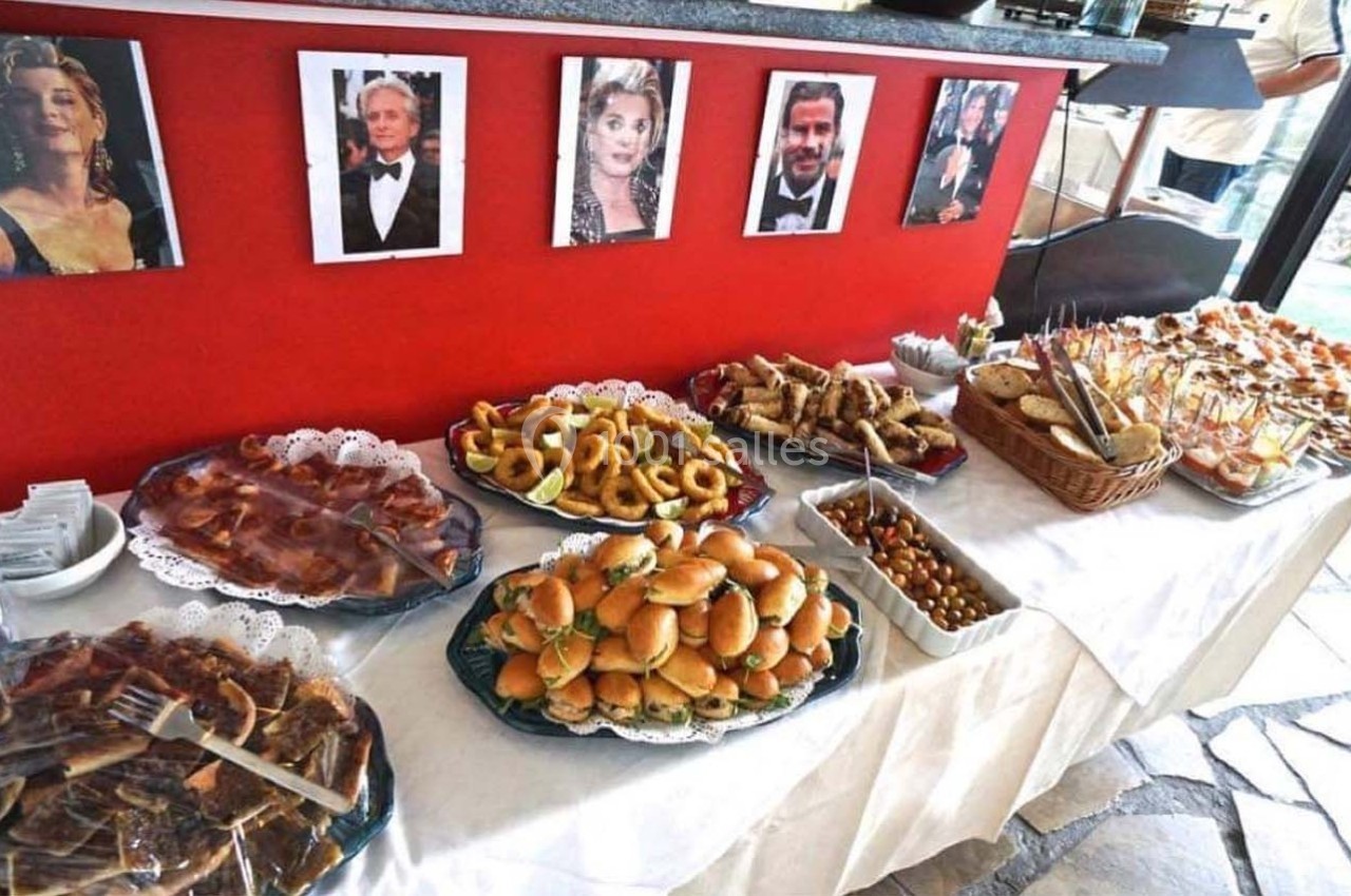 Buffet varié avec sandwiches, amuse-bouches, charcuterie et photos de célébrités accrochées sur un mur rouge.