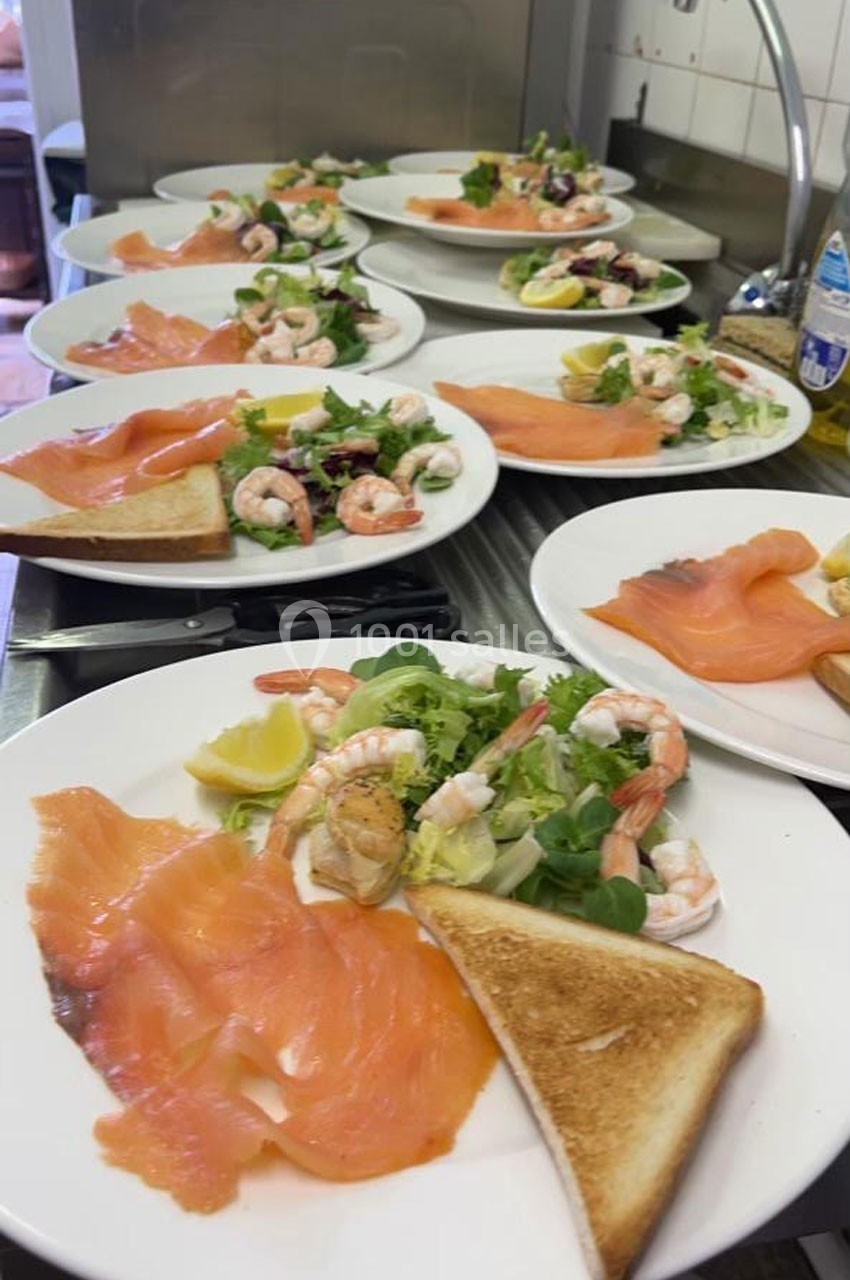 Assiettes garnies de saumon fumé, crevettes, salade verte, citron et toast, disposées sur un plan de travail en cuisine.